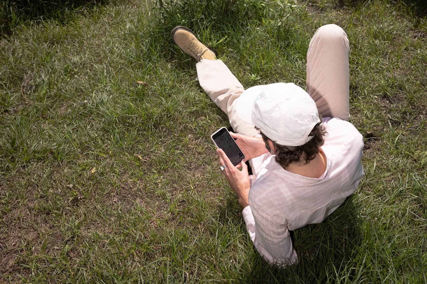 En man ligger i i gräset och tittar på sin mobil.