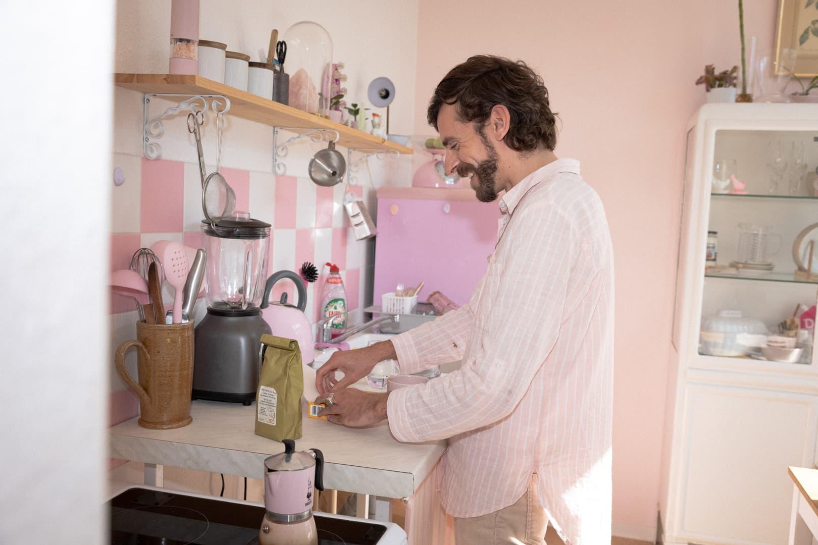Anyfinkund som står i ett rosa kök och och kokar kaffe. 