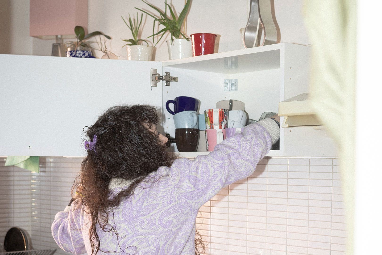En kvinna som sträcker sig efter en kaffekopp i köket.