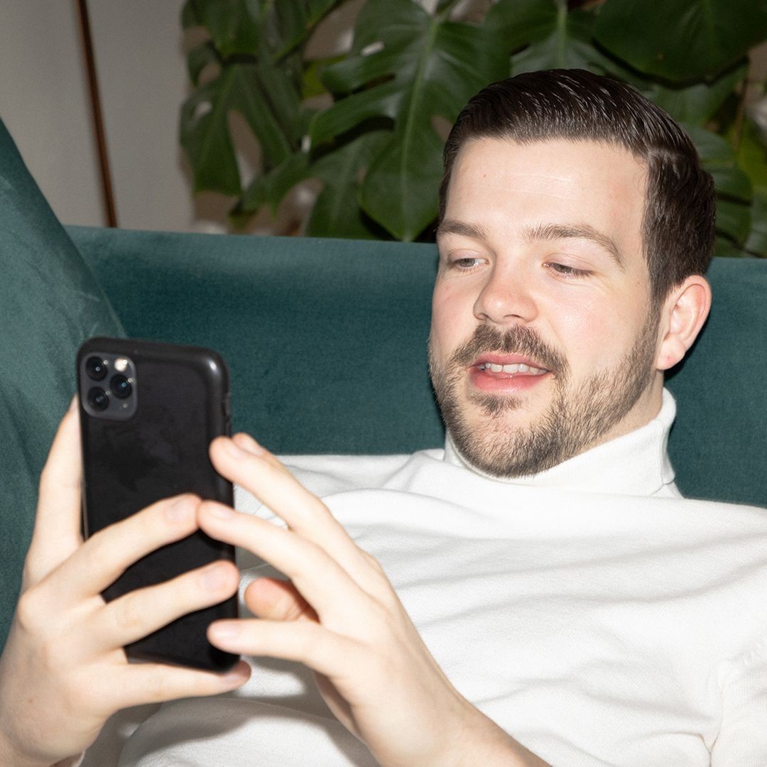 En man som ligger i en grön soffa och tittar på sin mobil.