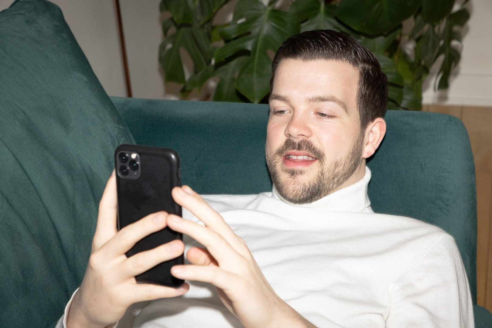 En man som ligger i en soffa och tittar på sin mobil.