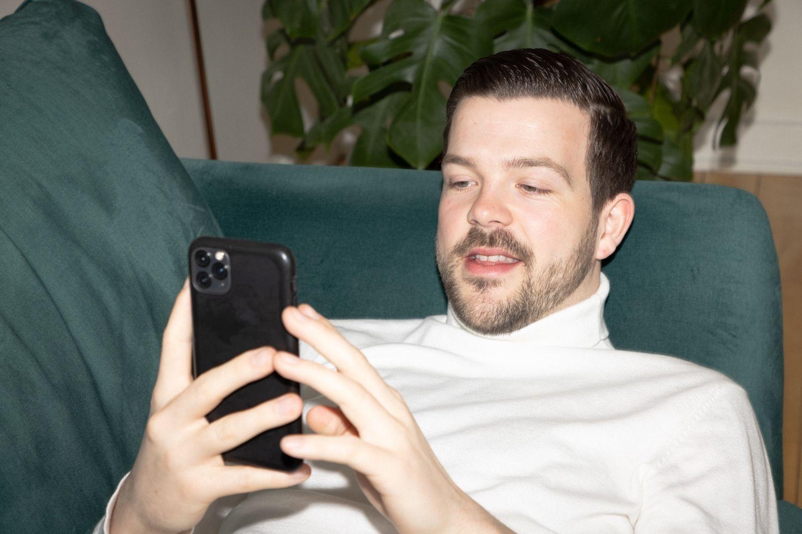 Mann auf Sofa mit Handy, benutzt die Anyfin-App